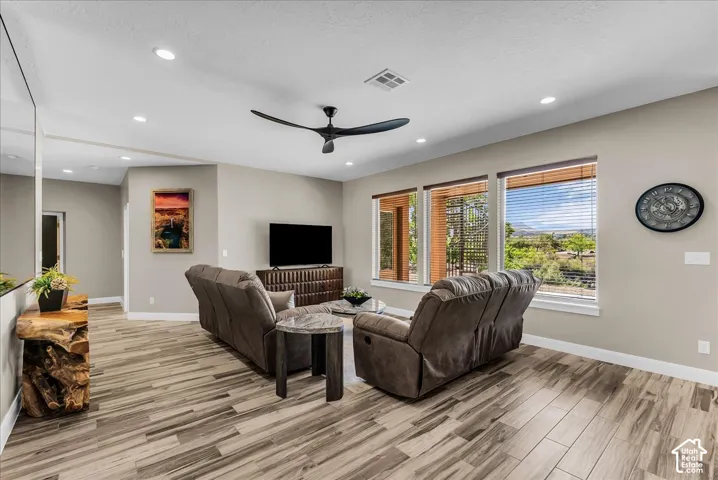 Sloped ceiling with recessed lighting, modern ceiling fan, wood-finish flooring, and multiple windows