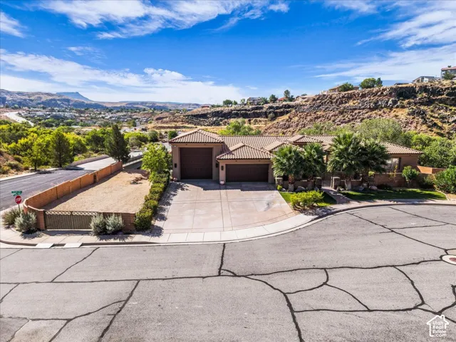 Mediterranean-style architecture with a tile roof, an attached two-car garage, mature landscaping, and an additional land parcel