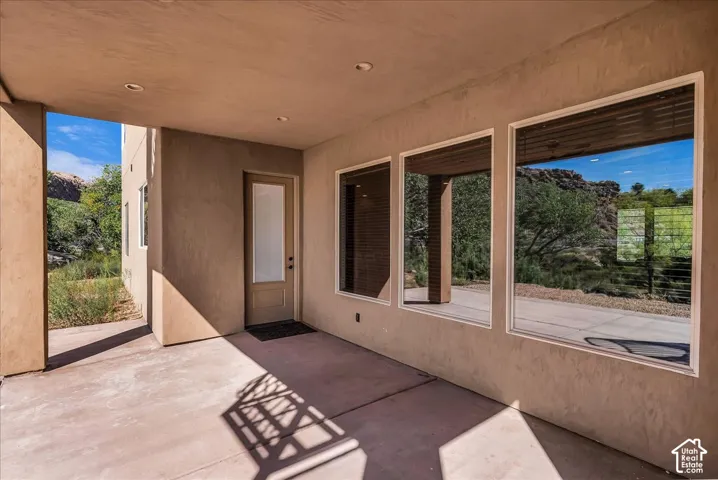 Covered patio with recessed lighting, smooth stucco exterior, three expansive windows, and a glass-paneled entry door