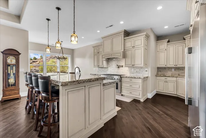 Gourmet kitchen featuring custom cabinetry, a spacious island with counter seating, stainless steel appliances, and wood-finish flooring