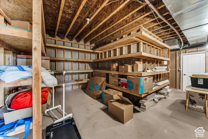 Unfinished basement featuring exposed wood beams, concrete flooring, and built-in wood shelving