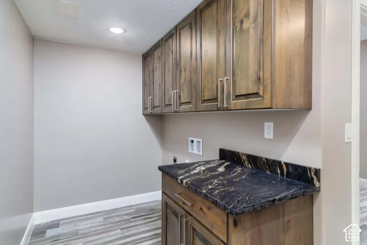 Wood-finish upper and lower cabinetry, patterned dark countertop, and wood-finish flooring