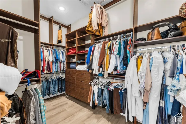 Built-in closet system with multiple hanging rods, integrated shelving units, drawer storage, and wood-finish flooring