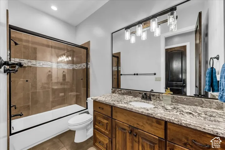 Built-in tub with sliding glass shower door, tiled shower surround with decorative accent band, wood-finish vanity with countertop, undermount sink, and wall-mounted light fixture