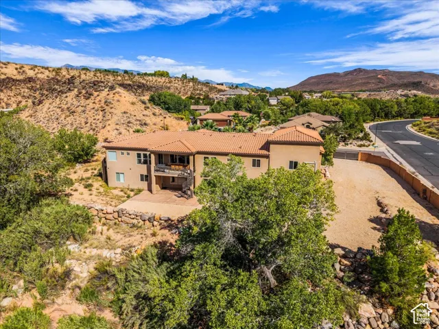 Terracotta tile roof, stucco exterior, upper-level balcony, lower-level patio, and natural landscaping with mature trees