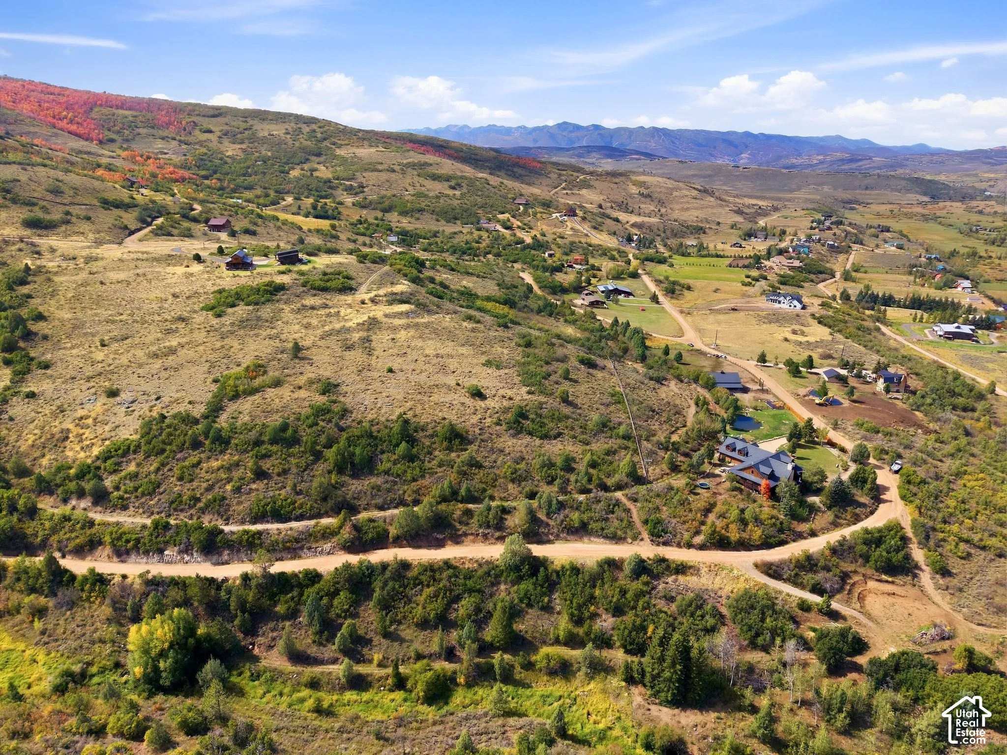 Expansive mountain terrain with varied foliage, featuring multiple residential structures and unpaved roadways