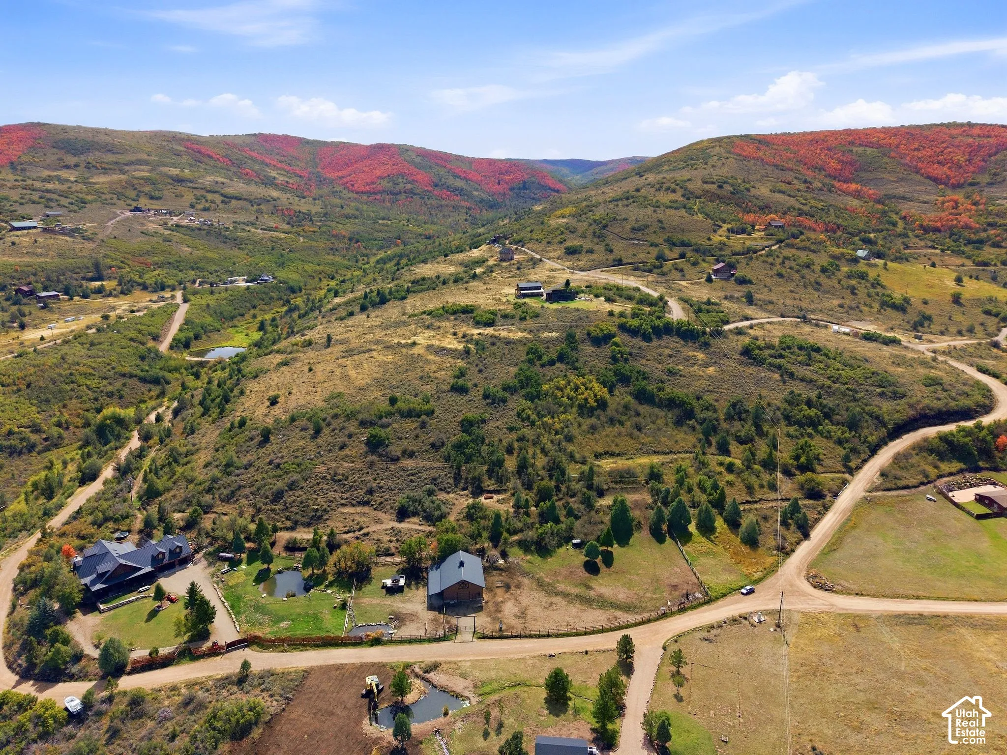Expansive property featuring multiple structures, a pond, and surrounding hillsides with diverse foliage