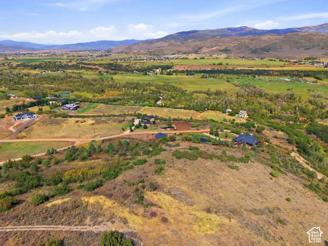 Expansive natural landscape featuring rolling hills, distant mountains, and scattered residences