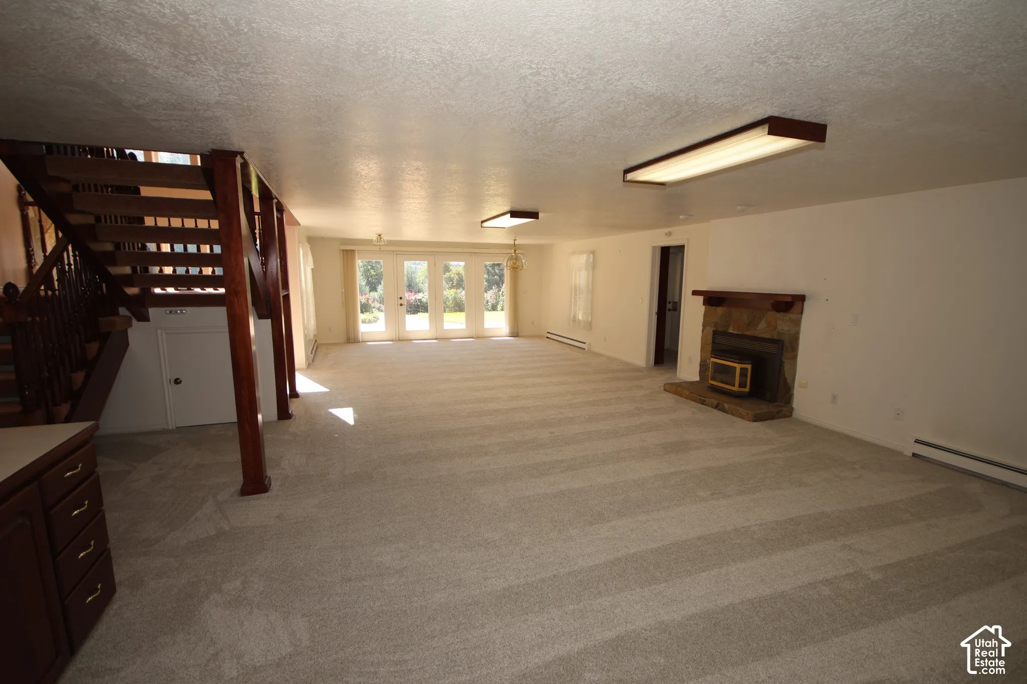 Spacious room with light-toned carpeting, a stone-faced fireplace with a wood mantle, and French doors