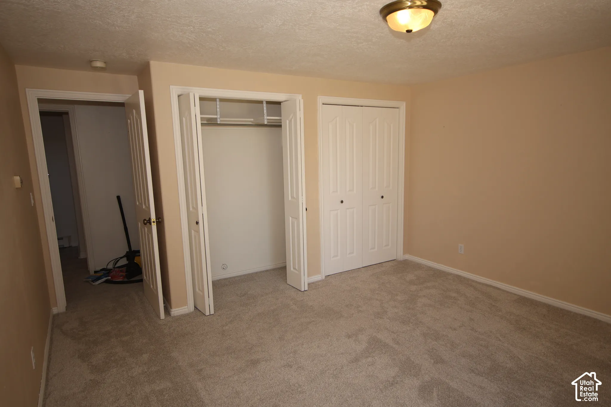 Neutral-toned walls, textured ceiling, flush mount ceiling light fixture, bi-fold closet doors, and carpet flooring