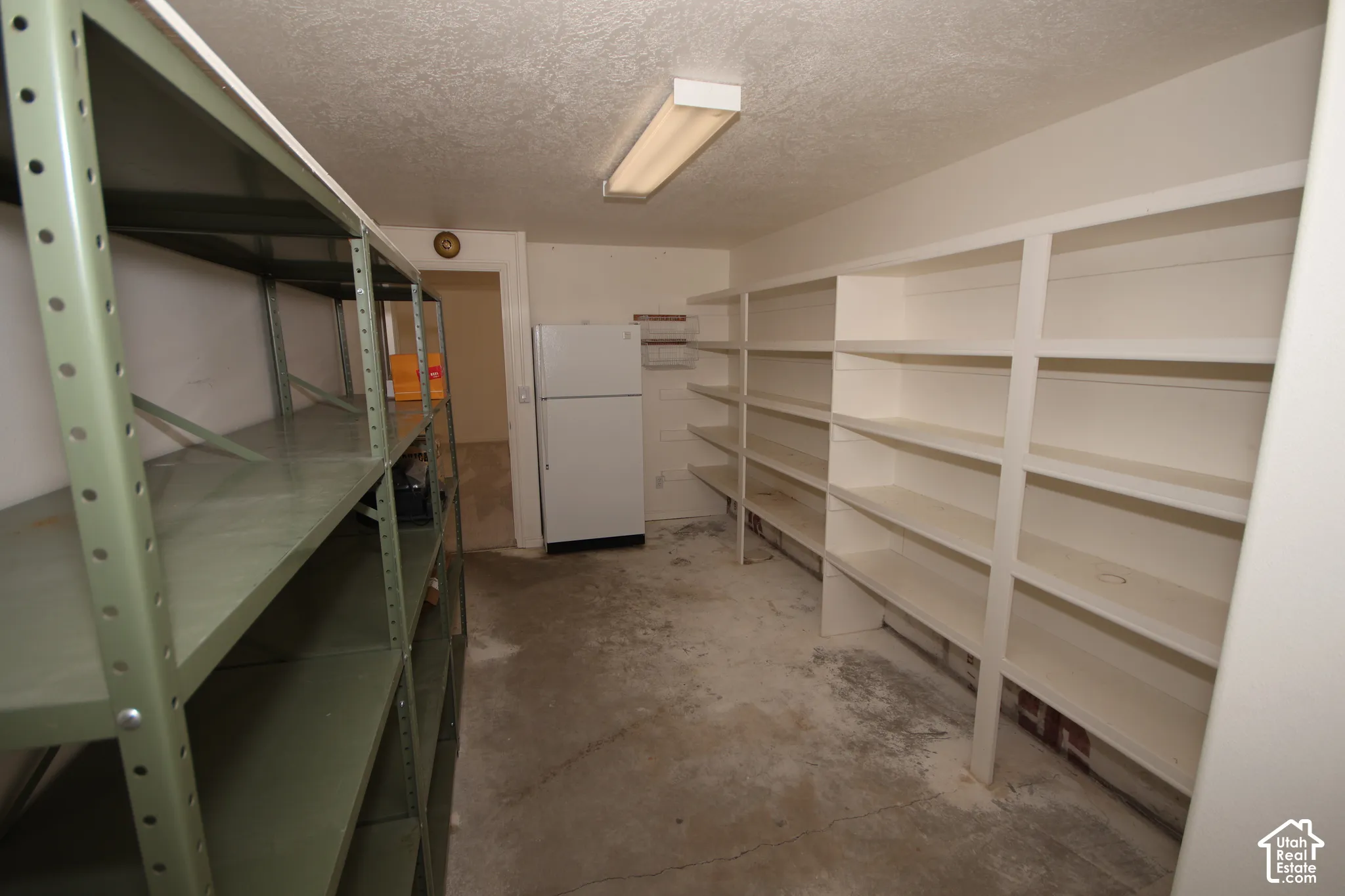 Built-in white shelving, metal shelving units, concrete flooring, and an overhead fluorescent light fixture