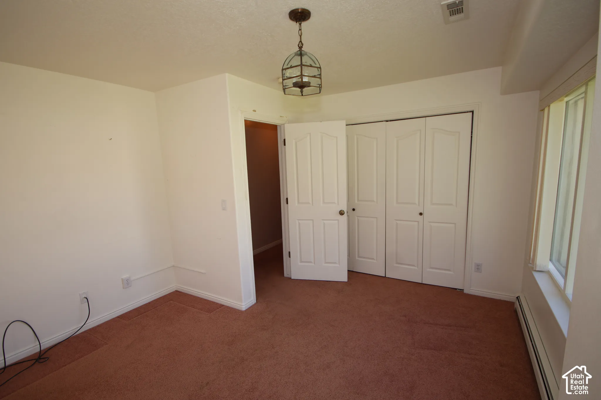 Neutral wall paint, textured ceiling, carpeted flooring, window with white frame, and a ceiling-mounted light fixture