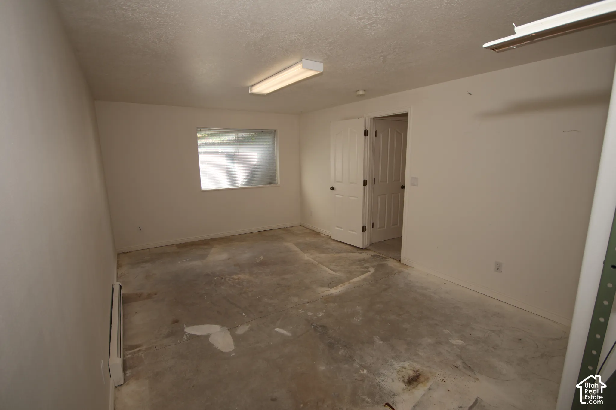 Window, white interior doors, fluorescent ceiling lighting, and baseboard heating