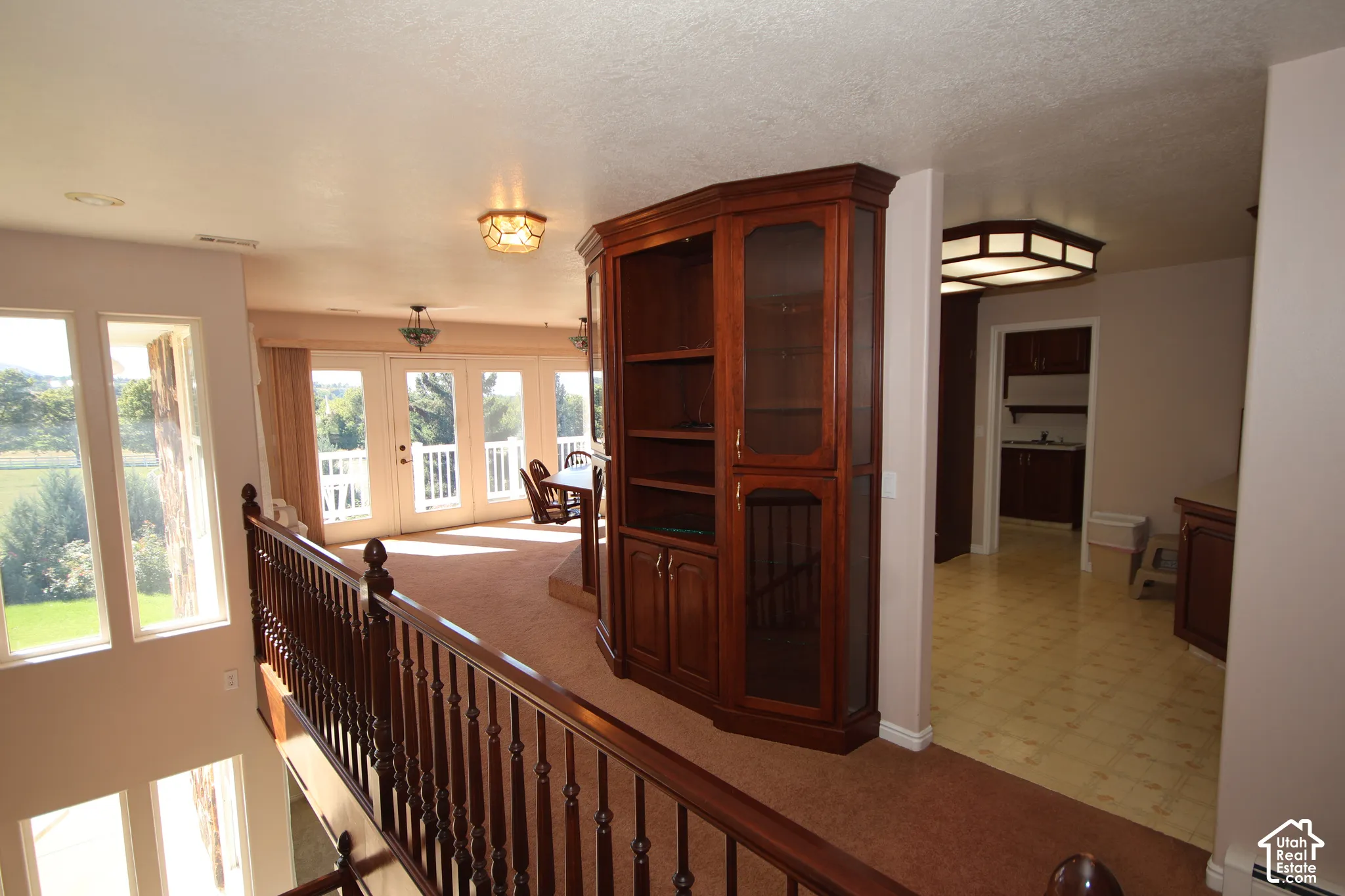 Upper level featuring a wood-finish railing, built-in shelving with glass-front cabinets, and multiple windows