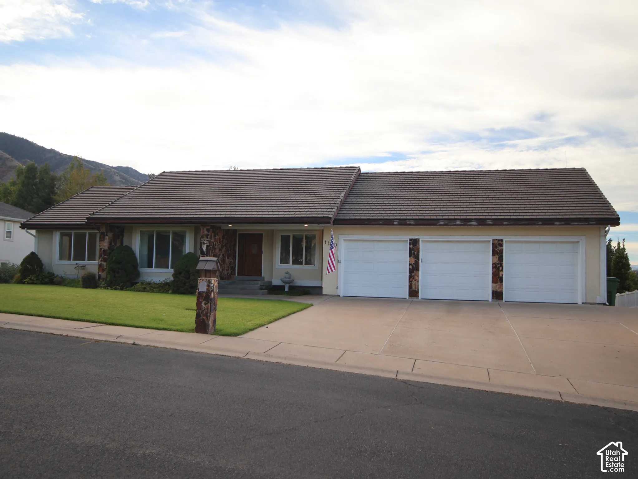 Stucco exterior with stone accents, brown tile roof, three-car garage, manicured lawn, and concrete driveway