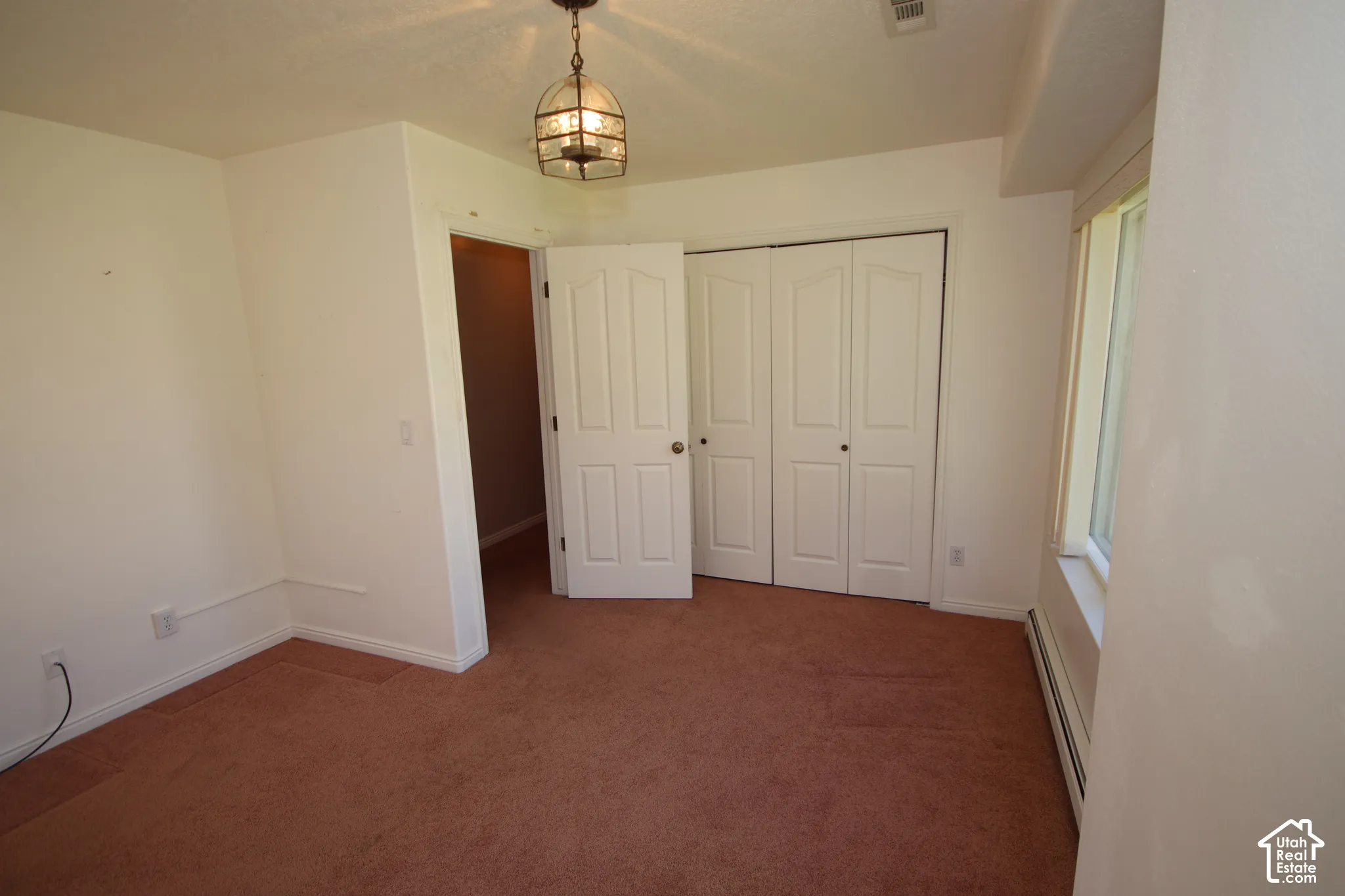 Carpeted room featuring a ceiling-mounted light fixture, white walls, and a window