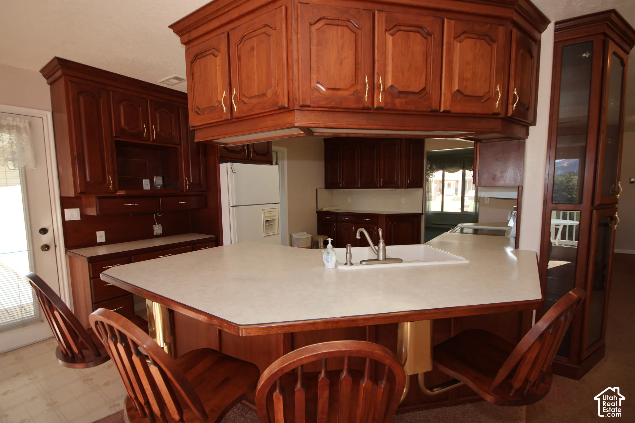 Kitchen featuring extensive wood cabinetry, a built-in display cabinet, a central island with an integrated sink, and light-toned countertops