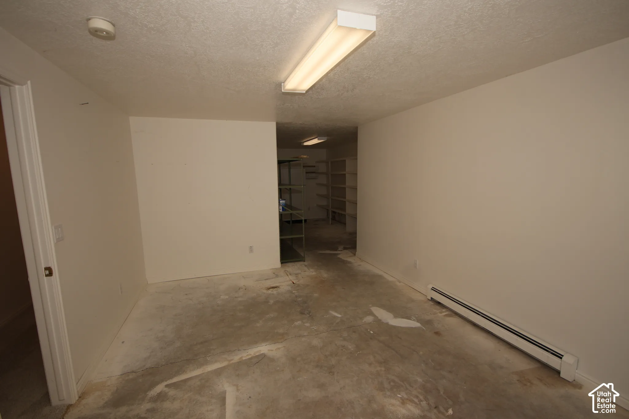 Unfinished space with smooth painted walls, fluorescent overhead lighting, and built-in shelving units