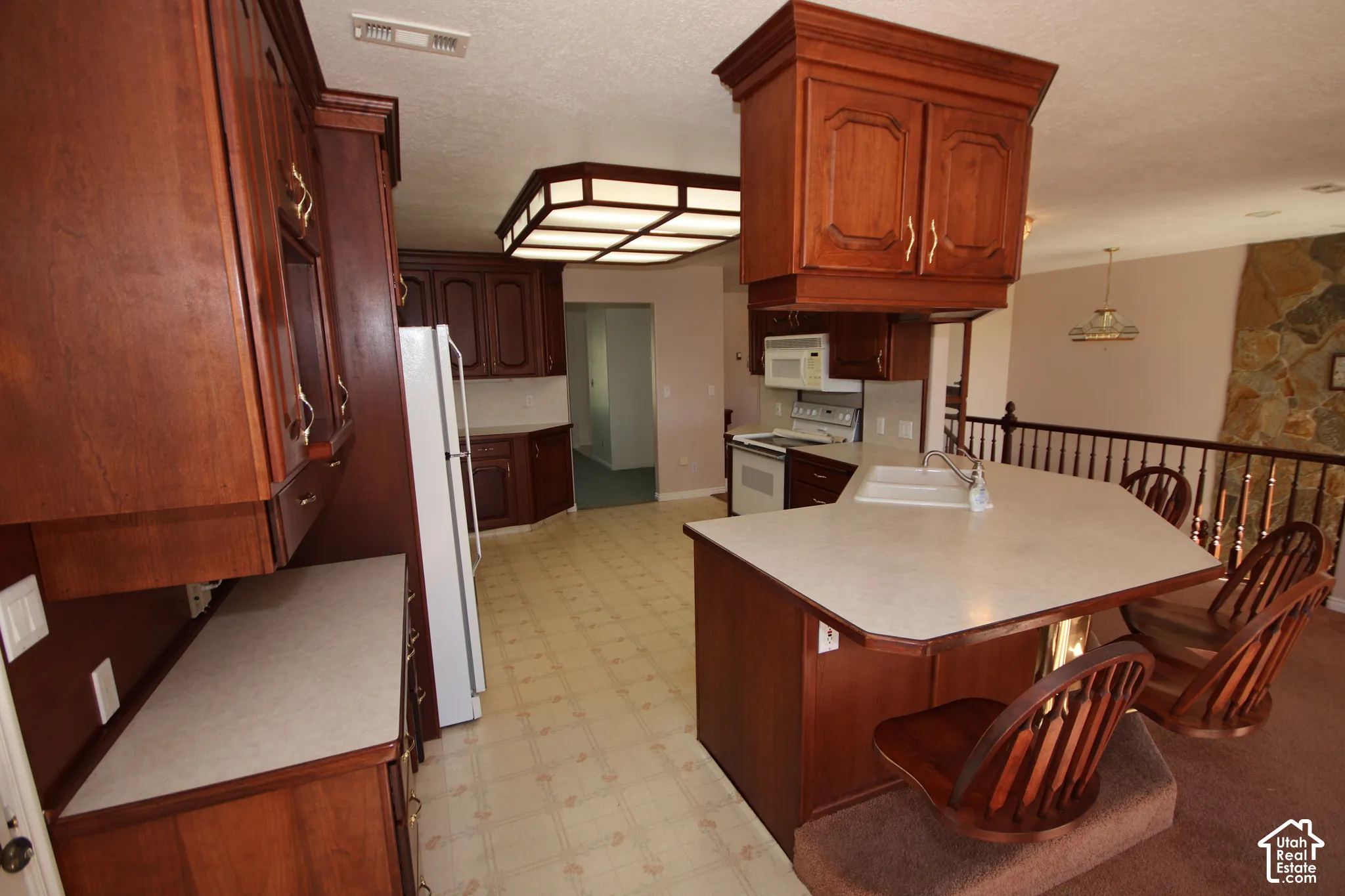 Kitchen featuring wood cabinetry, a central island with integrated sink, white appliances, and patterned floor tile