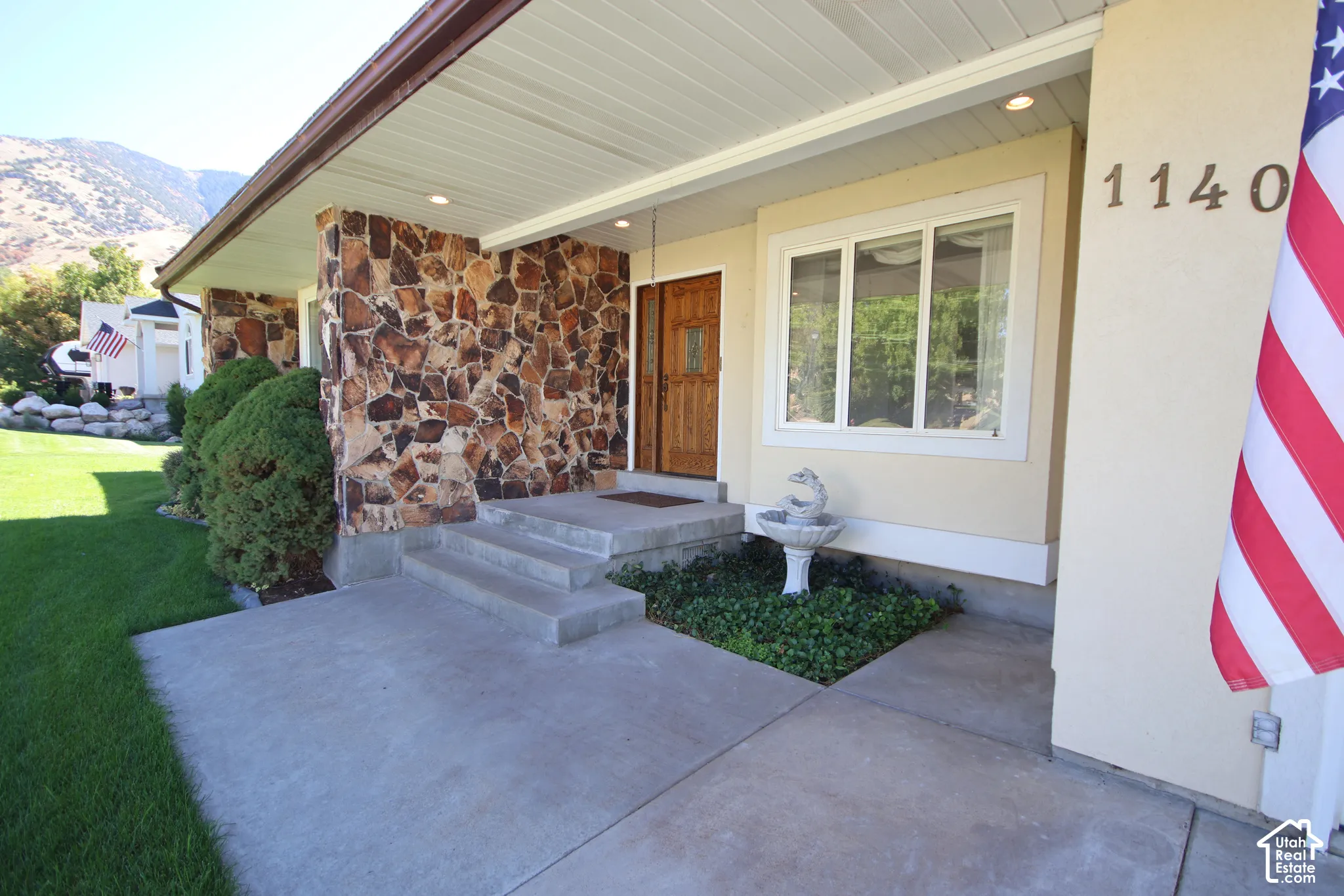 Stone-clad exterior accent, wood-finish entry door, concrete steps, built-in window, and a decorative fountain