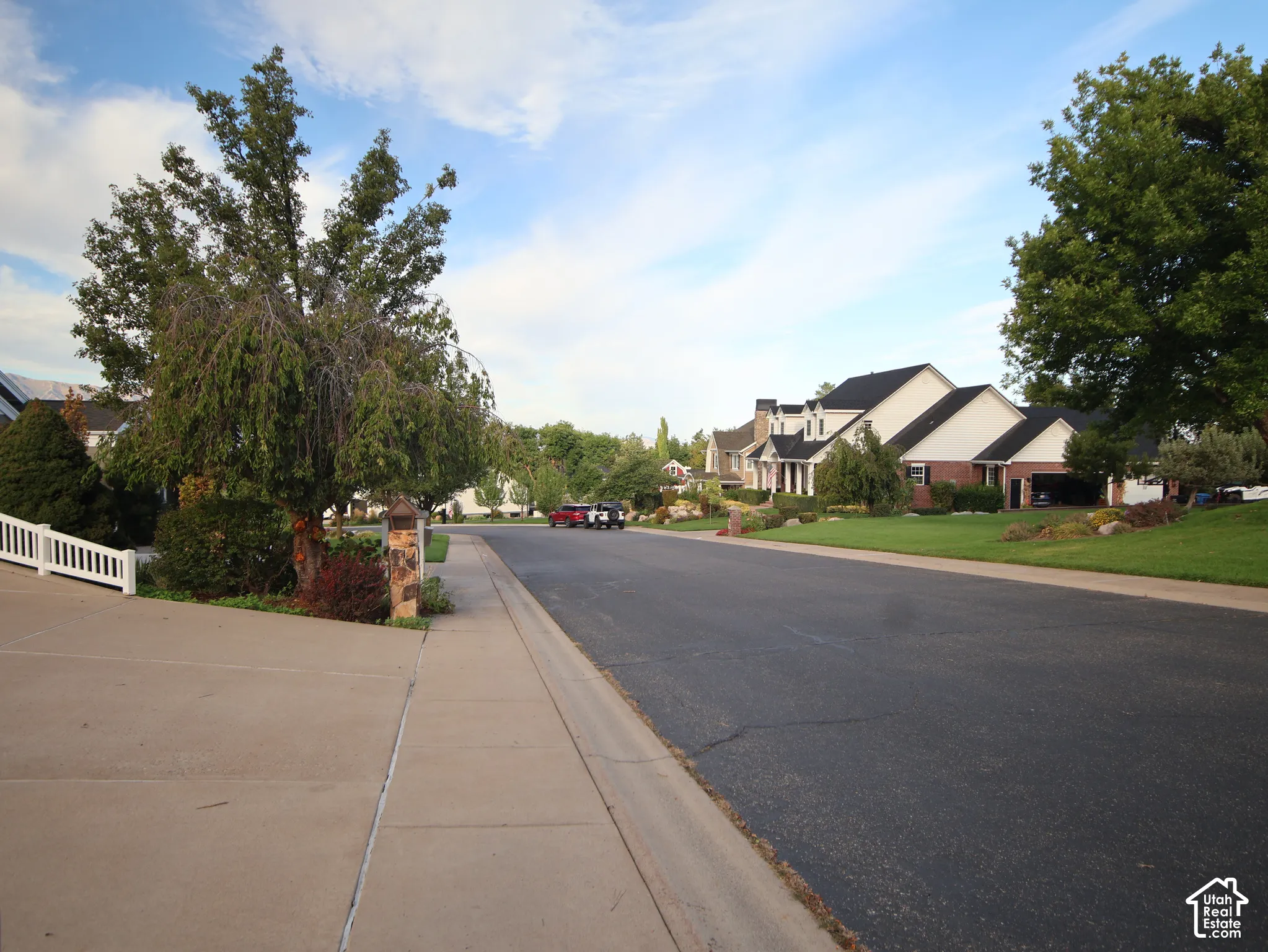 Residential street with paved road, concrete sidewalk, and manicured green lawns