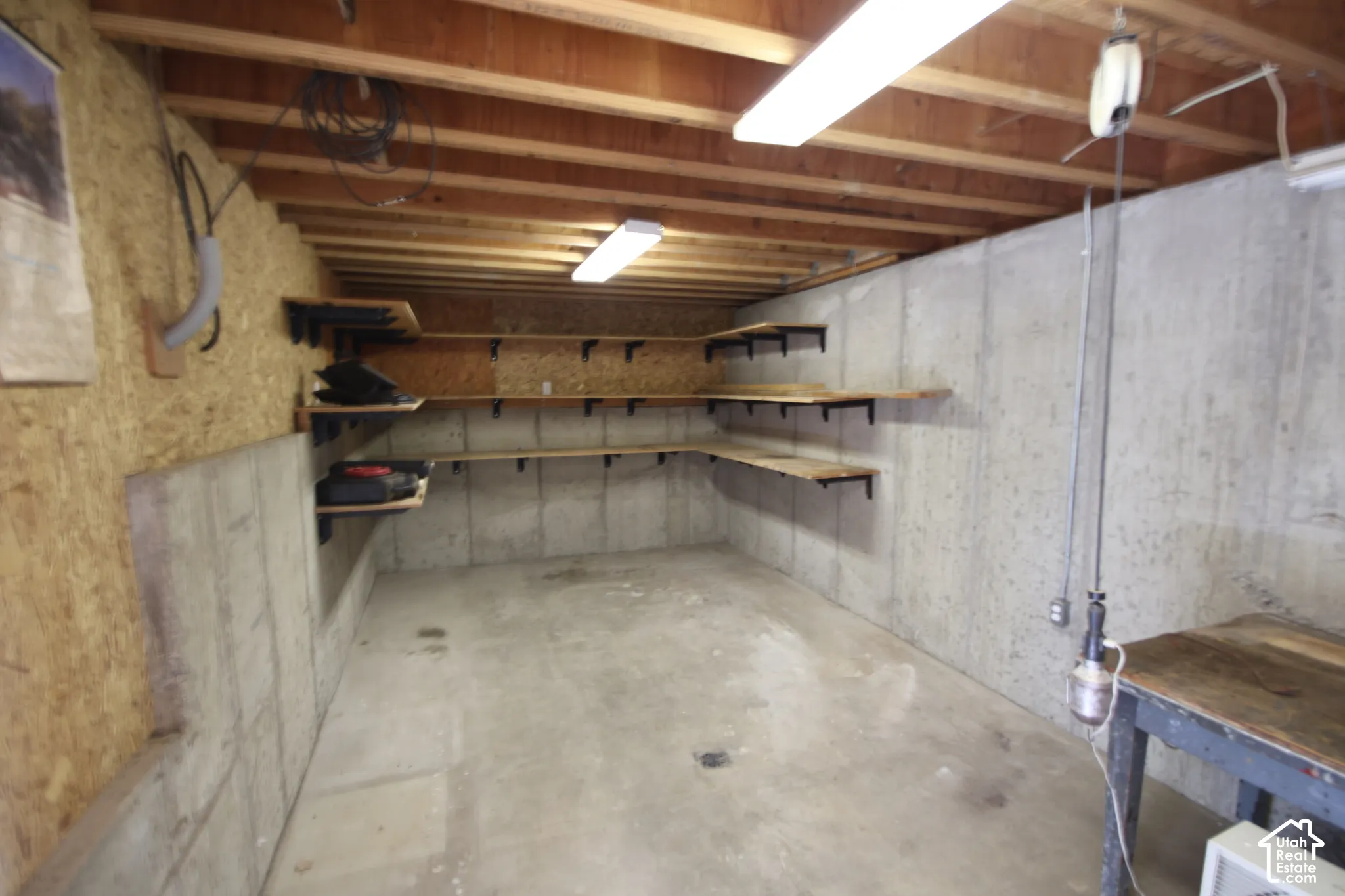 Concrete flooring, exposed wood beam ceiling, built-in wall shelving, and fluorescent lighting fixtures
