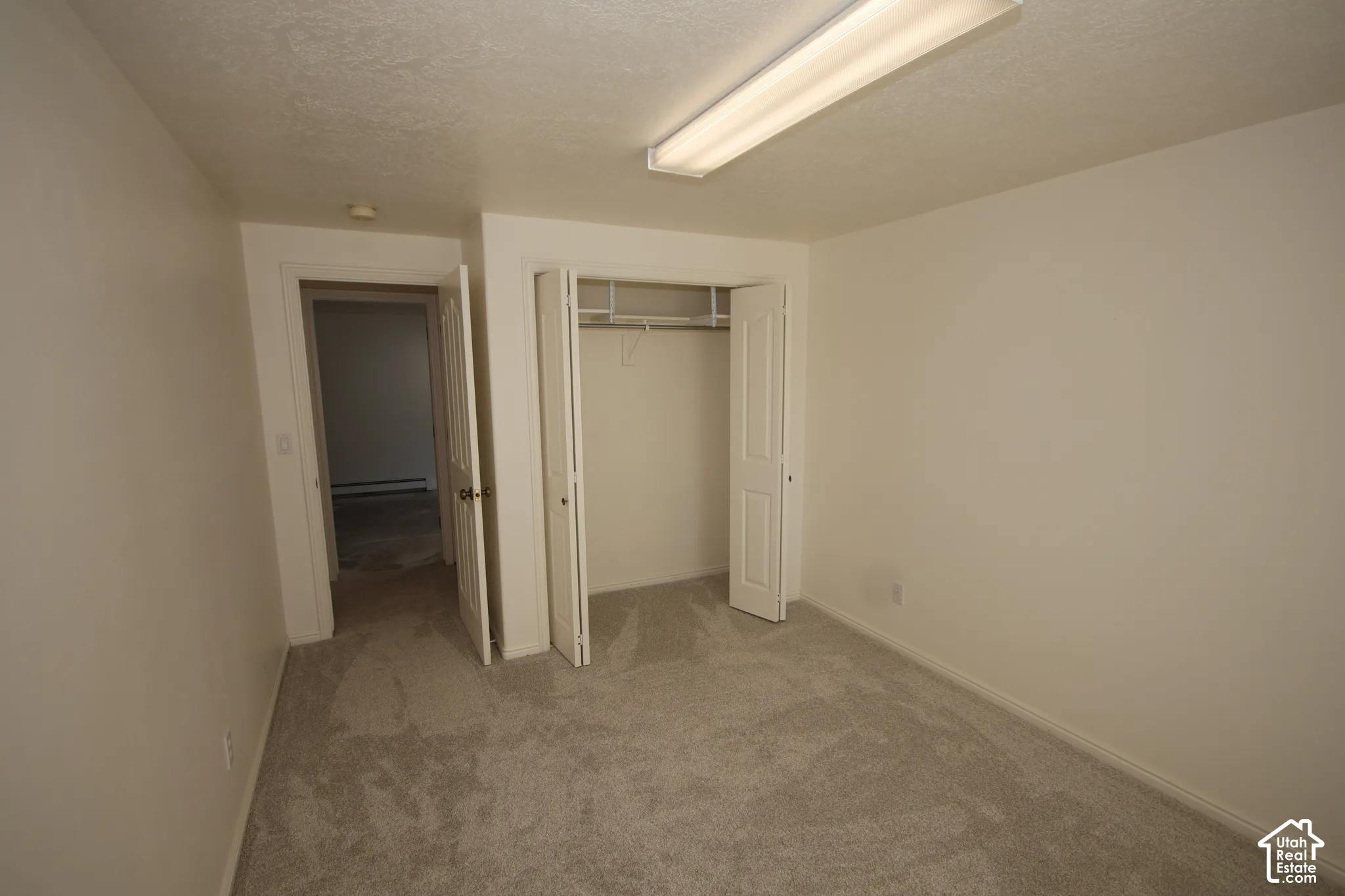 Neutral wall paint, textured ceiling, fluorescent ceiling lighting, soft grey carpeting, and bifold closet doors