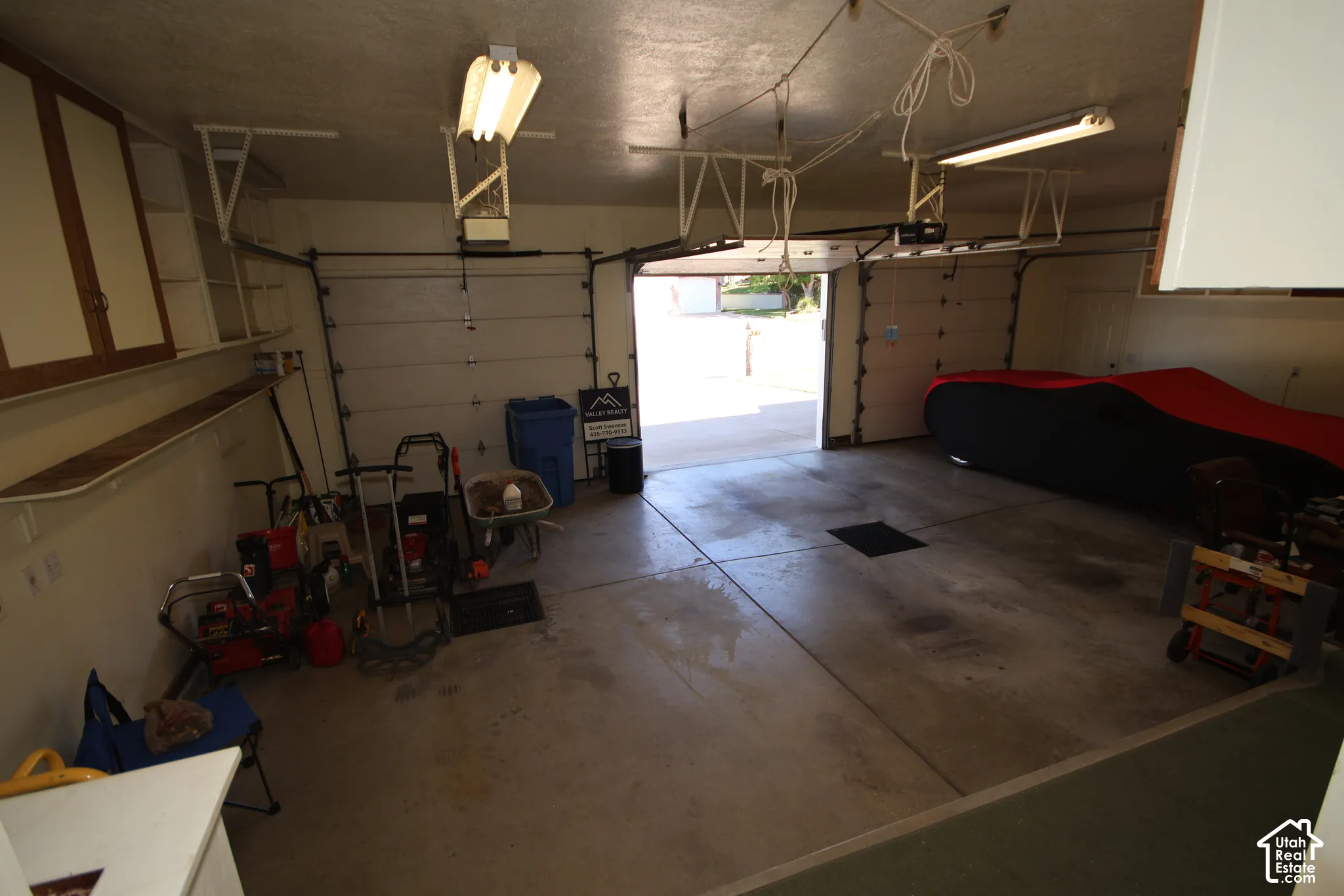 Two-car garage with concrete flooring, built-in shelving, and overhead fluorescent lighting