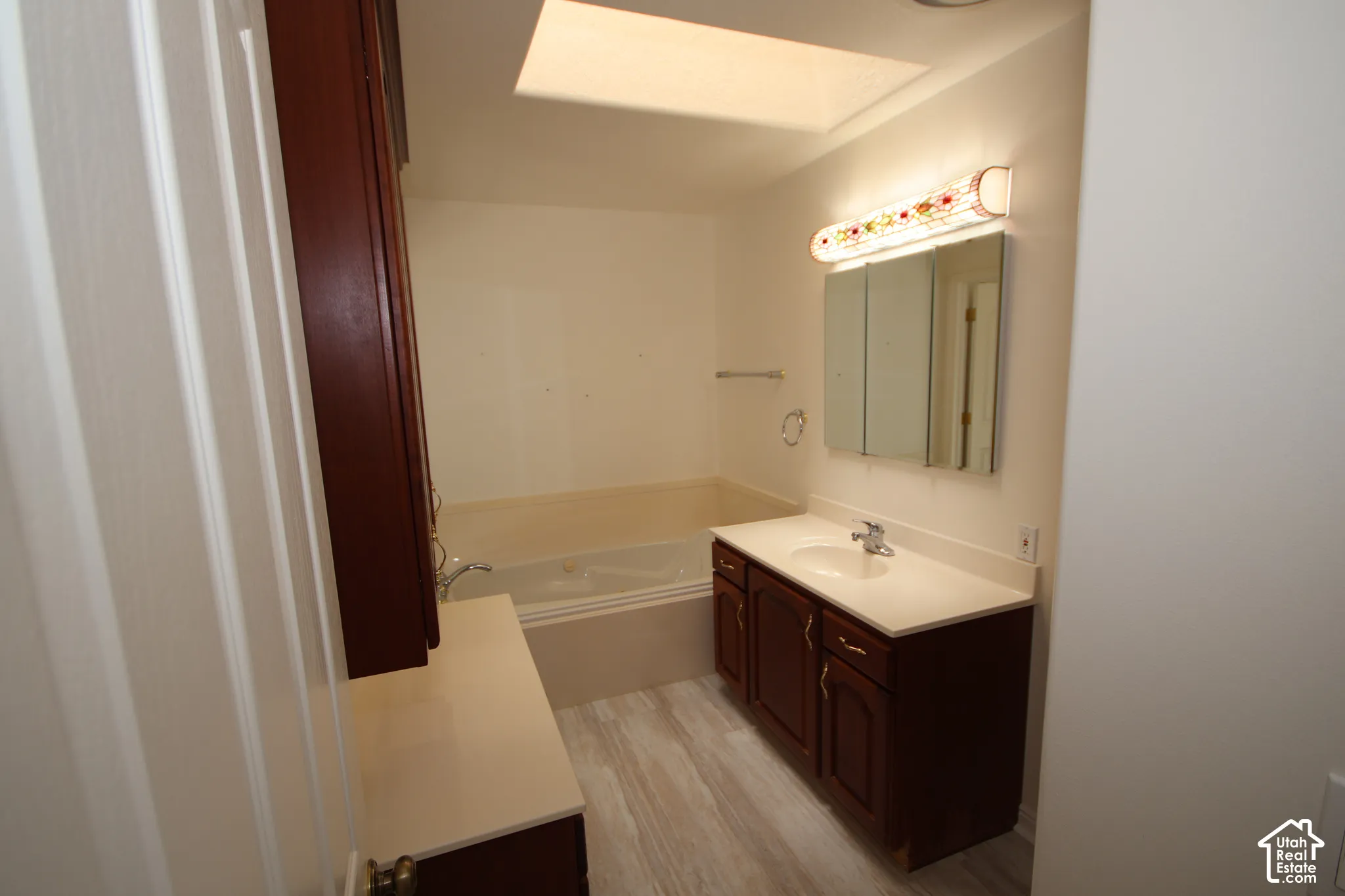 Recessed ceiling light, white soaking tub, vanity with integrated sink, wood-finish flooring, and built-in medicine cabinet