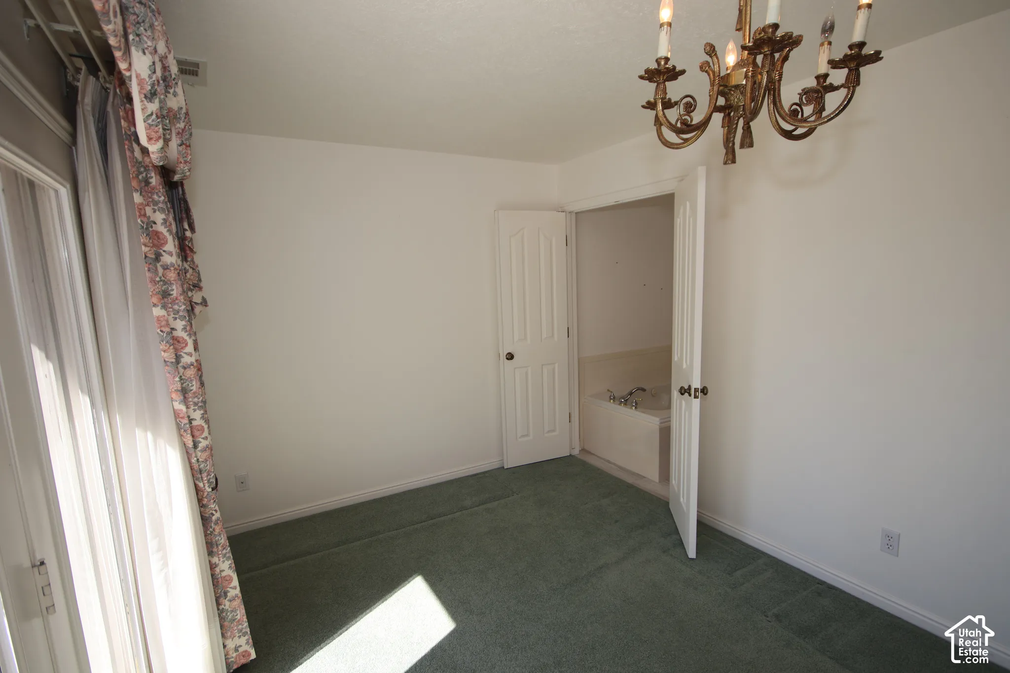 White walls with wall-to-wall carpeting, an ornate brass chandelier, white panel doors, and a built-in tub