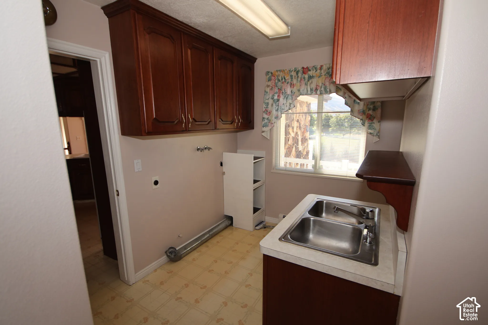 Wood-finish cabinetry, dual basin stainless steel sink, light-toned countertop, and window