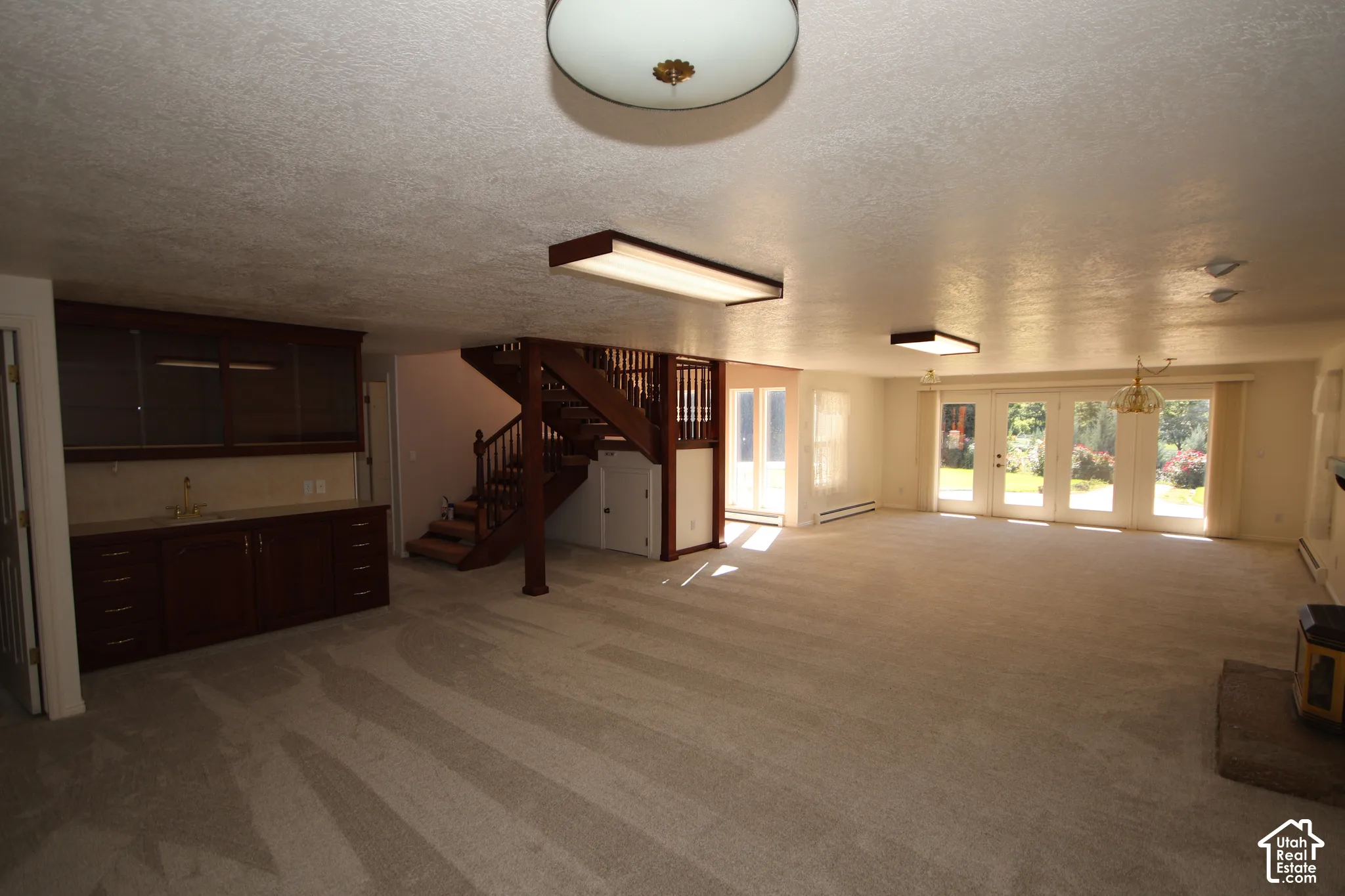 Expansive room featuring a wet bar with built-in cabinetry, a wooden staircase, and multiple sets of French doors leading to exterior