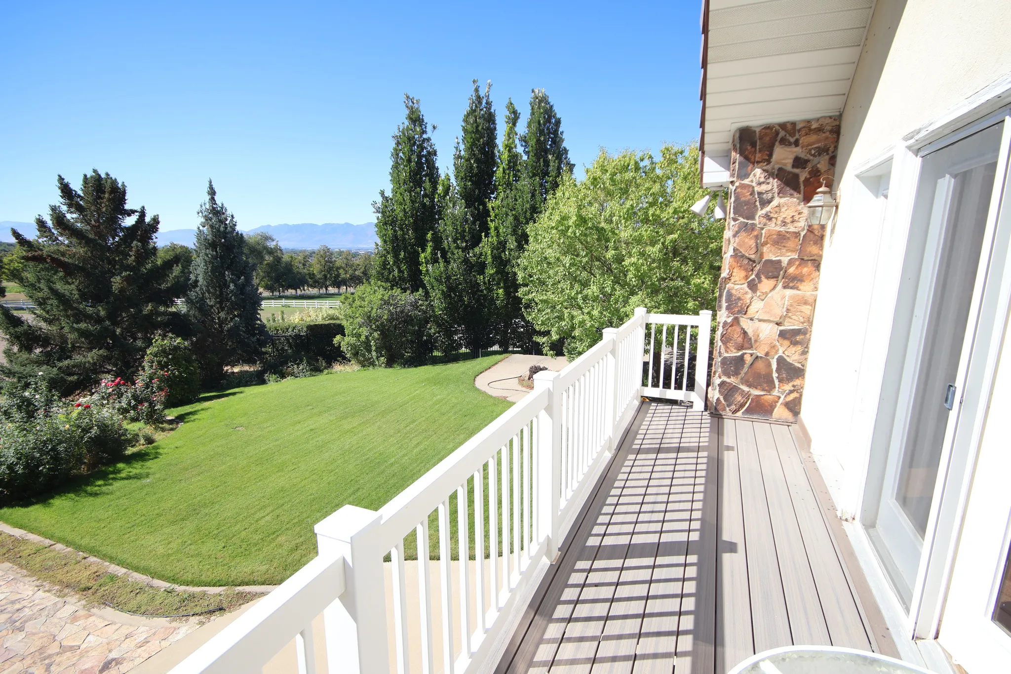 Balcony with composite decking and white railing, featuring a sliding glass door and stone accent wall