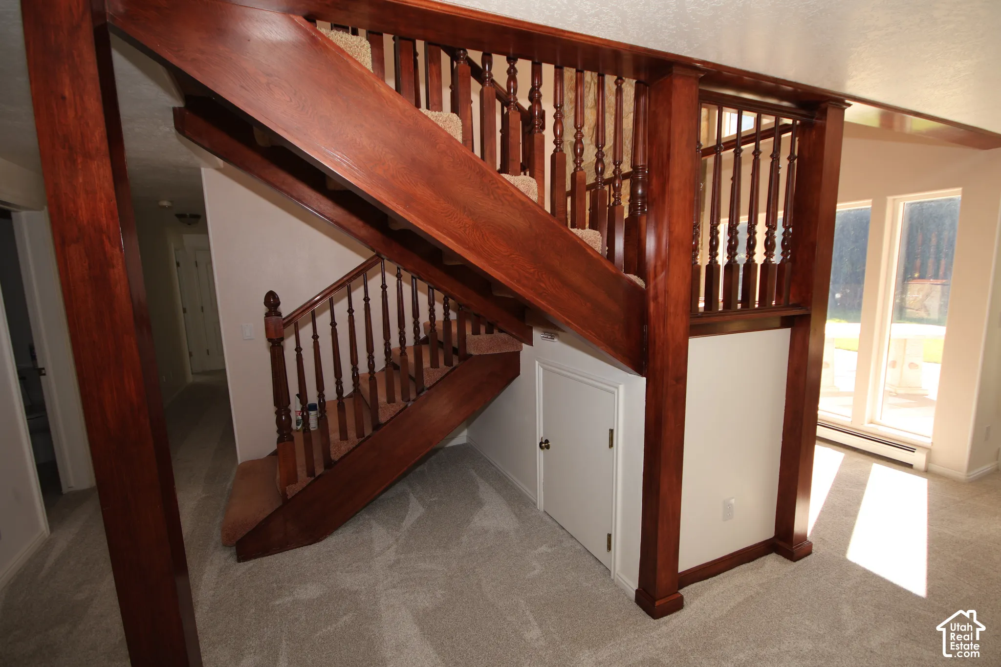 Hardwood staircase with ornate balusters, carpeted treads, and a built-in under-stair storage door