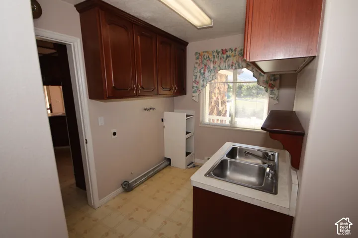Wood-finish cabinetry, dual basin stainless steel sink, light-toned countertop, and window