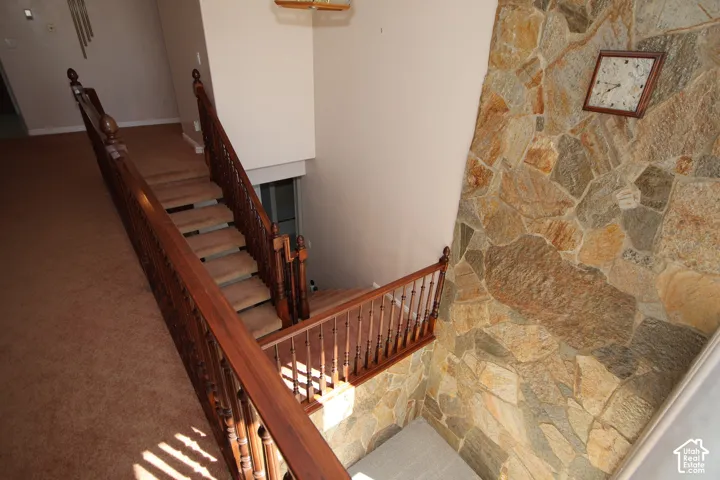 Spacious stairwell featuring a stone accent wall, wood banisters, and carpeted stairs