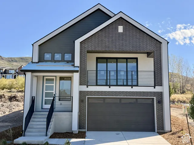 Contemporary facade featuring mixed materials, an integrated garage, a second-story balcony with sliding glass doors, and a modern entry door with sidelight