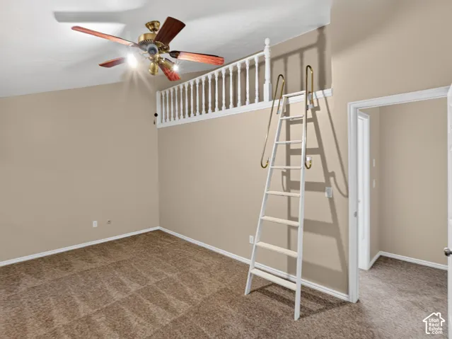 Carpeted flooring, neutral wall tones, ceiling-mounted fan, white balustrade, and a white ladder with brass-finish handrails