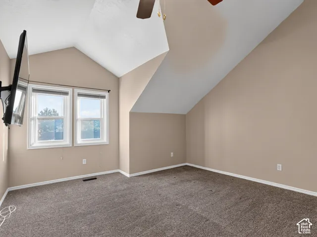 Vaulted ceiling with a ceiling fan, dual windows, and carpeted flooring