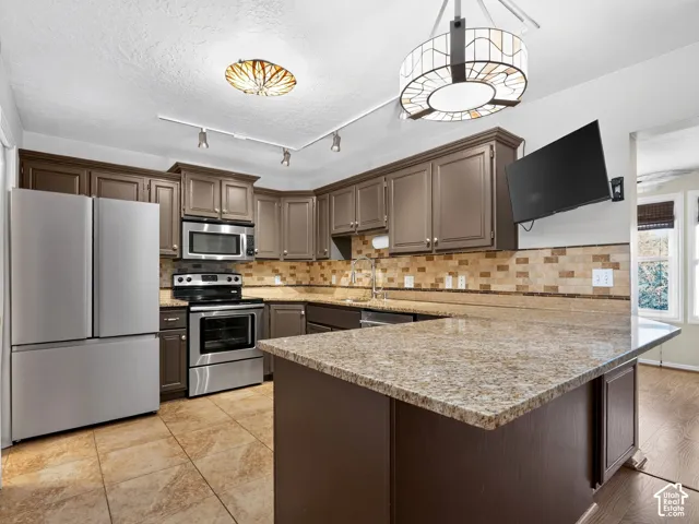 Kitchen featuring stainless steel appliances, granite countertops, wood cabinetry, tile flooring, and a decorative tile backsplash