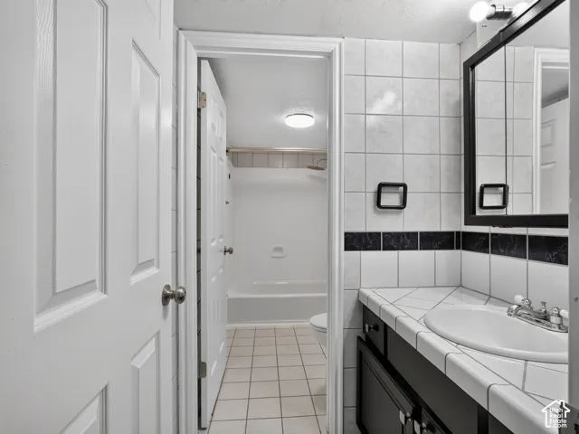 White panel doors, tiled vanity countertop with integrated sink, black framed mirror, white tiled walls with a decorative black border, and a white bathtub