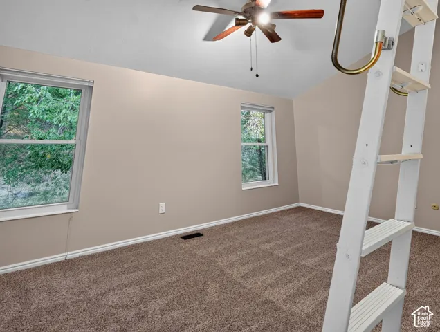 Angled ceiling, two windows, ceiling fan with wood-finish blades, carpeted flooring, and a built-in ladder with a handrail