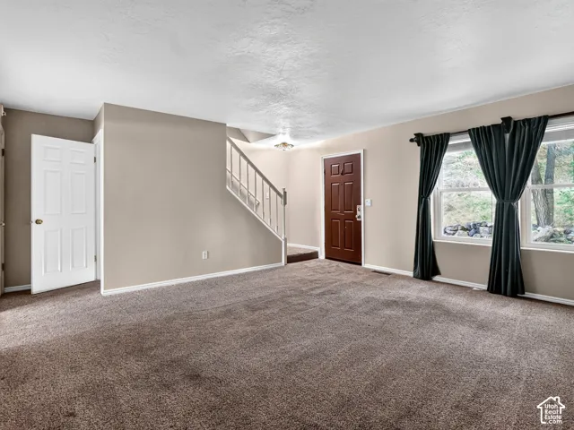 Carpeted room with a staircase featuring a white railing, a brown paneled entry door, and large windows