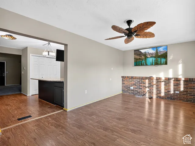 Wood-finish flooring, half-wall brick accent, ceiling fan with decorative blades, and a built-in breakfast bar with a granite-look countertop