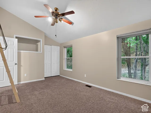 Vaulted ceiling with a ceiling fan, dual windows, and plush carpet flooring