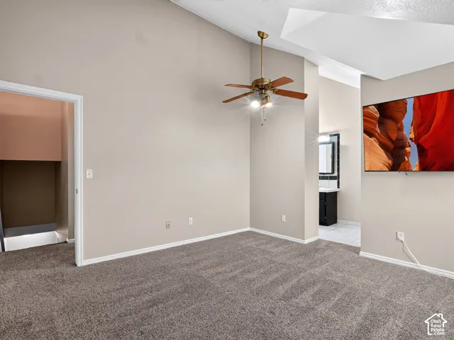 Vaulted ceiling with a brass-finish ceiling fan, neutral wall paint, and gray carpet flooring