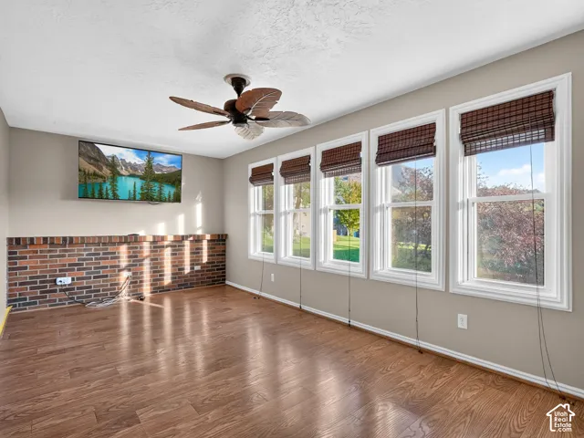 Wood-finish flooring with a partial brick accent wall and multiple windows featuring woven blinds