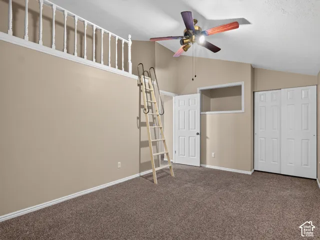 Vaulted ceiling, ceiling fan, carpet flooring, white trim, and a white interior door