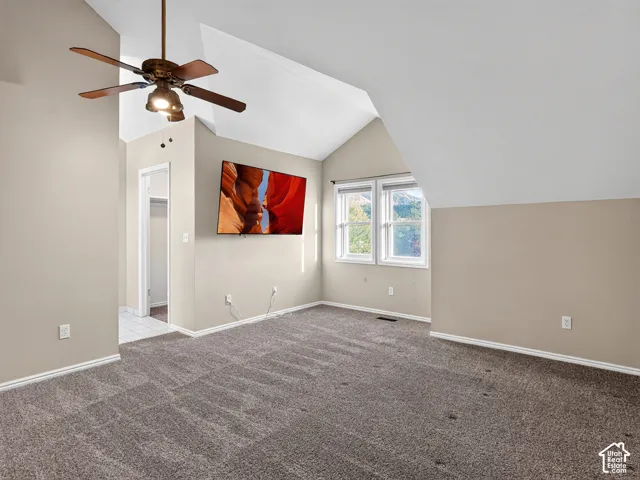 Vaulted ceiling with a ceiling fan, plush carpeting, multiple windows, and a wall-mounted television