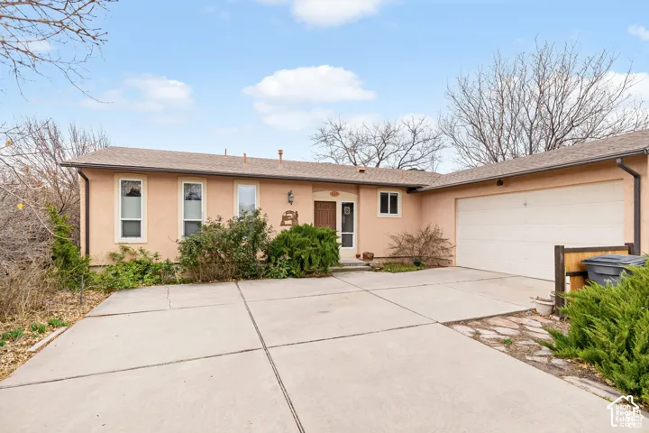 Stucco exterior with a pitched roof, attached garage, and mature landscaping